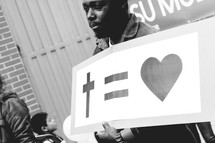 A man holding a sign cross = heart 