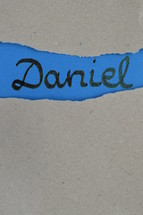 book Daniel - torn open kraft paper over blue paper with the name of the prophetic book Daniel