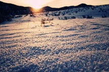 Snow-covered terrain and the silhouette of mountains at sunrise. 