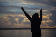 a silhouette of a woman on a beach with raised hands 