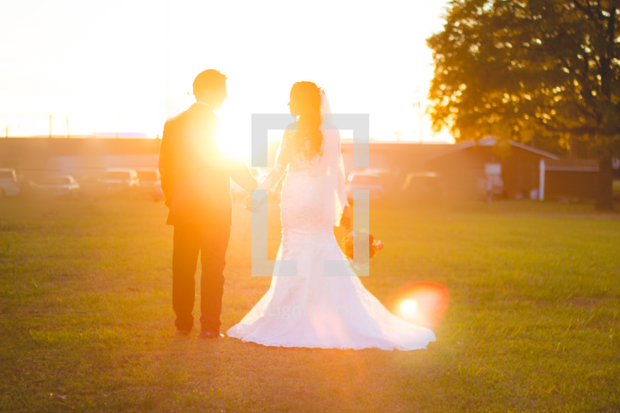 a bride and groom standing under intense sunlight in grass outdoors 
