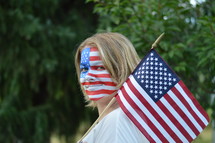 woman with American flag painted on her face - young blond woman with the american flag painted all over her face and carrying a flag over her shoulder