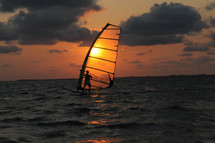 Sunset behind a sail surfer on the ocean water.