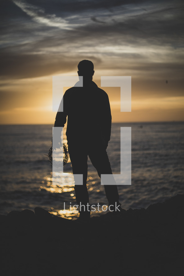 a man holding a crown of thorns on a shore at sunset 