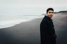 a man standing on a black sand beach 