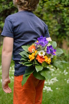 a child holding a bouquet of flowers behind his back 