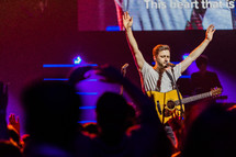 A musician on stage with arms raised in praise.