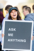 A laughing woman holding a sign reading, "Ask Me Anything."