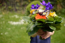 a boy child holding a bouquet of flowers for mom 