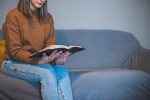 a woman reading a BIble on a couch 
