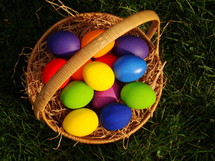 Multicolored Easter eggs in a basket, in the grass.
