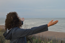 a woman standing on a beach with raised hands 