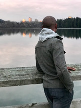 a man looking over a railing across a lake at city buildings 