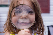 a girl looking through a magnifying glass with a reflection of the sky
