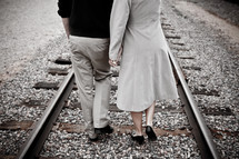 Rear view of a young couple walking down a railroad track
