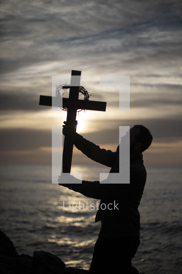 man holding up a cross with crown of thorns at sunset 