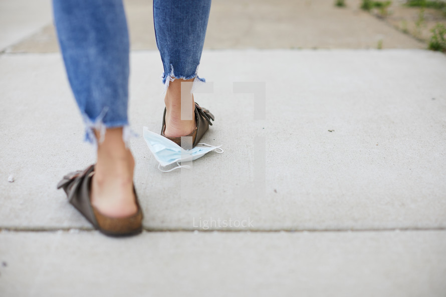 a woman stepping on a discarded mask 