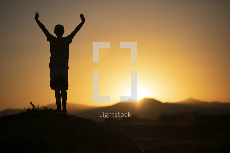 teen boy standing in warm sunlight with arms raised