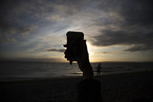 taking a picture of the sunset with a cellphone on a beach 