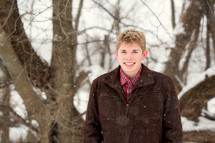 a young man standing in the woods in falling snow 