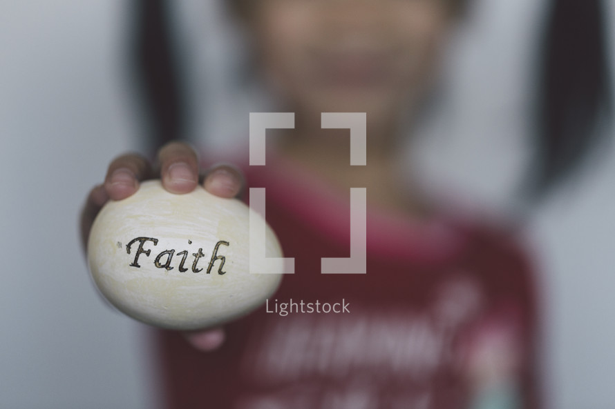 girl holding an Easter egg stamped with the word faith 