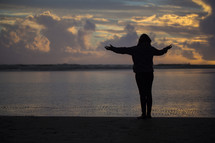 a woman standing on a beach with outstretched arms 