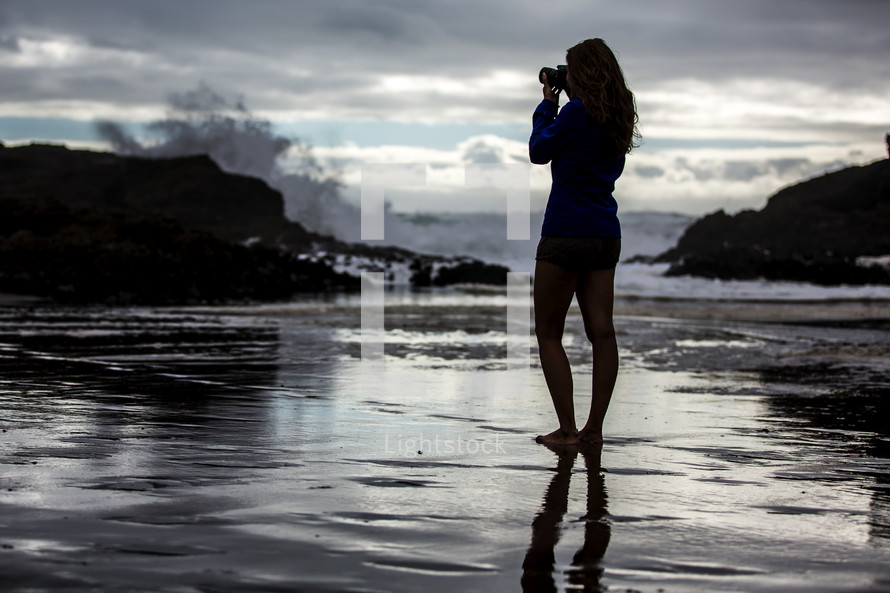 woman with a camera standing in shallow water taking a picture 