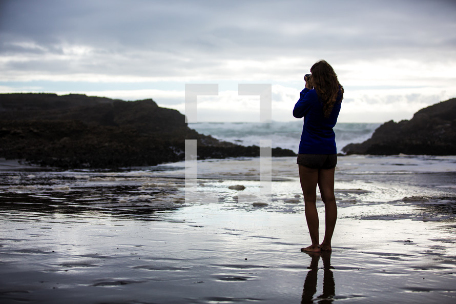 woman standing in shallow water with a camera taking a picture 
