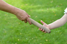 woman giving the relay baton to the next generation into a child's hand