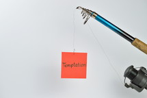 the word temptation on a red piece of paper hanging from a fishing line 