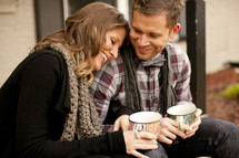 couple holding coffee mugs outdoors sitting on a step 