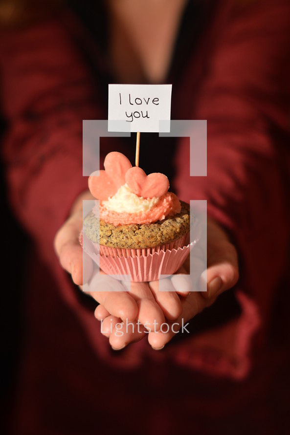 Woman offering a cupcake with pink hearts and a sign saying I LOVE YOU. 
