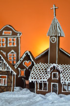 home made gingerbread village in front of orange background on white snowlike velvet as advent decoration