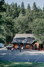 youth playing basketball in front of a log cabin 