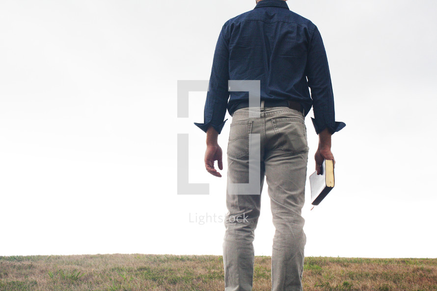 a man standing in a field holding a Bible 