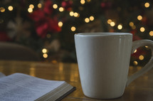 mug and open Bible on a coffee table and Christmas tree in the background 