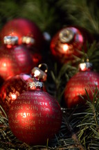 Red Christmas balls with gold lettering on evergreen branches.