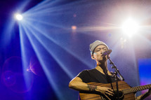 A man singing and playing a guitar under stage lights.