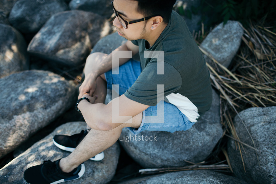a man sitting on rocks alone thinking 