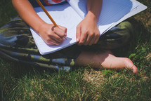 boy writing in a notebook sitting in the grass