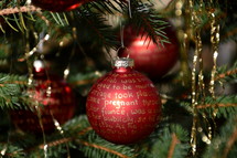 The Nativity story written in golden letters on red Christmas ornament bulbs. 
