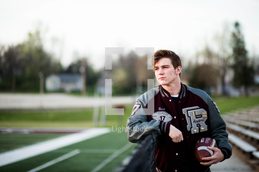 a young man in a letter-jacket holding a football 