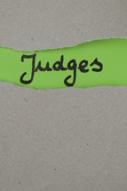 torn open kraft paper over green paper with the name of the book of Judges