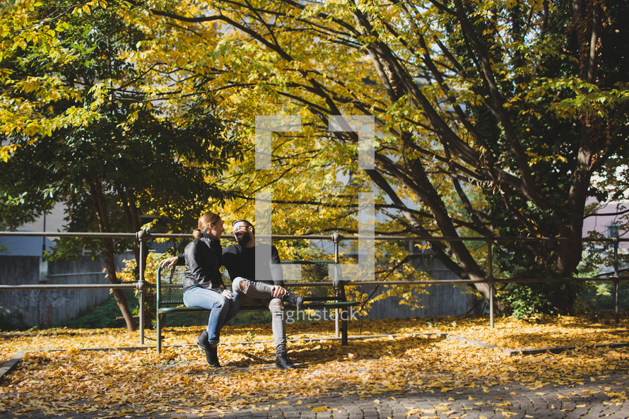 a couple sitting on a park bench in fall 