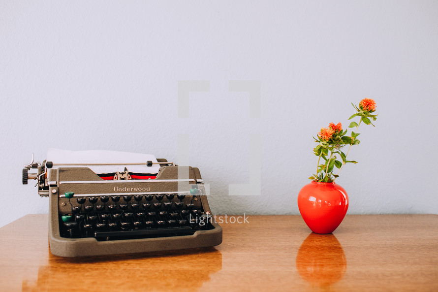 typewriter and flowers in a vase on a desk 