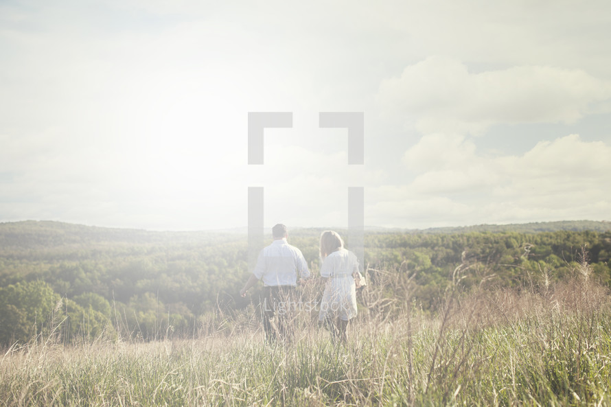 Couple walking through a field surrounded by hills.