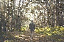 a man standing alone on a path in a forest with a backpack 