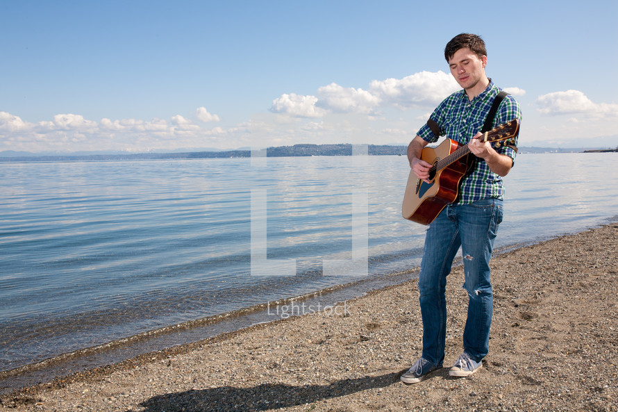 man playing a guitar on the shore of a lake