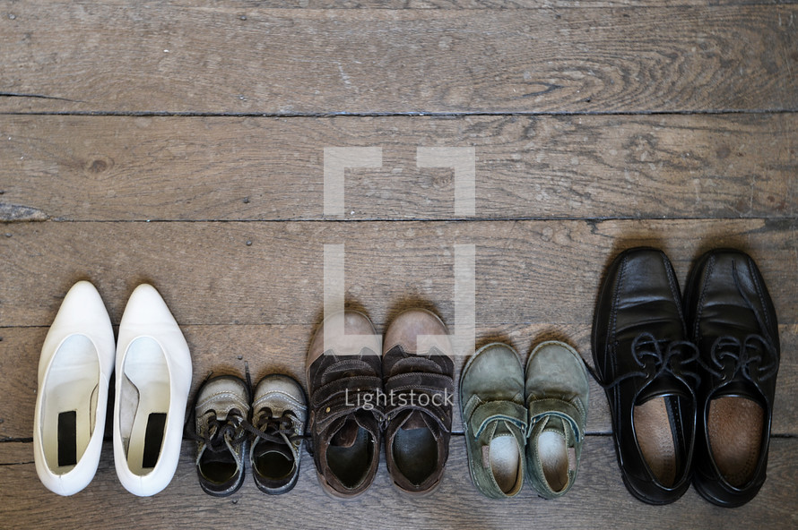 Family's shoes lined up on a wood floor. 
