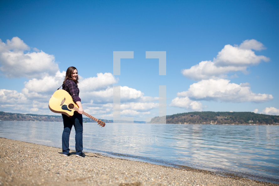 woman holding a guitar standing at the edge of a lake